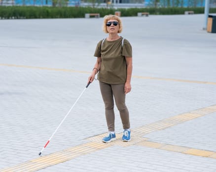 An elderly blind woman walks with a cane along a tactile tile