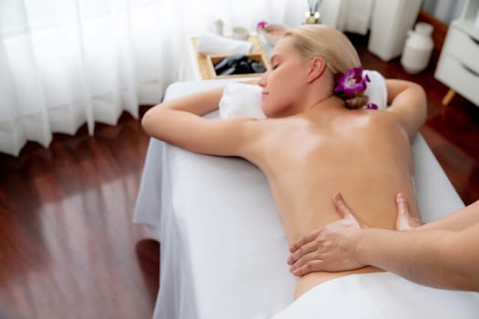 Caucasian woman customer enjoying relaxing anti-stress spa massage and pampering with beauty skin recreation leisure in day light ambient salon spa at luxury resort or hotel. Quiescent