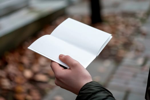 Hand holding white blank book for mockup isolated city background..