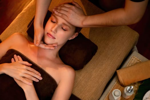 Caucasian woman enjoying relaxing anti-stress head massage and pampering facial beauty skin recreation leisure in warm candle lighting ambient salon spa in luxury resort or hotel. Quiescent