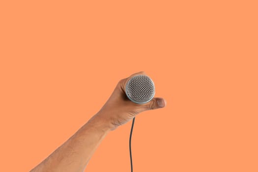 Black male singer hand holding a microphone isolated on orange background. High quality photo