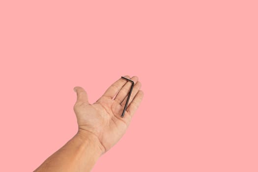 Black male hand holding an allen key isolated on pink background, cutout. High quality photo