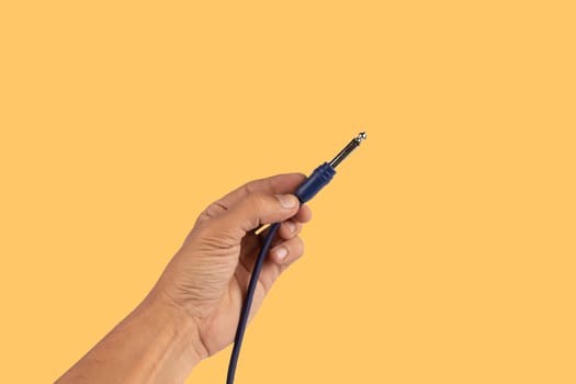 Black male hand holding an audio Jack cable isolated on yellow. Guitar cable. High quality photo