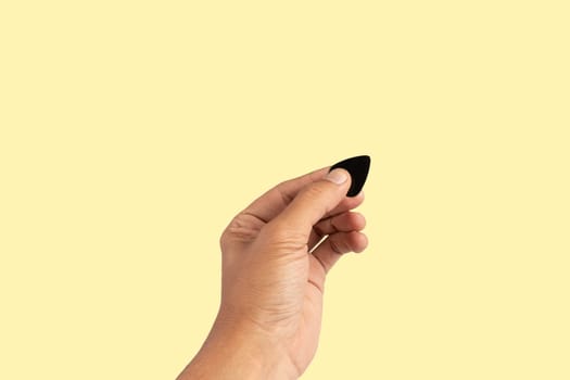 Black male hand holding a guitar pick isolated on yellow background. High quality photo