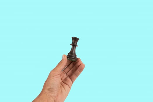 Black male hand holding a black queen chess figure isolated on cyan background. High quality photo