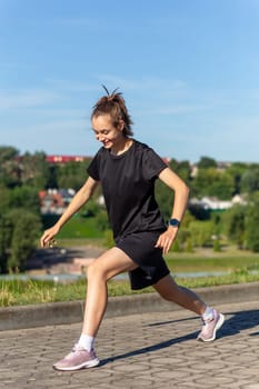 Young, fit and sporty girl in black clothes stretching after the workout in the urban city park. Fitness, sport, urban jogging and healthy lifestyle concept.