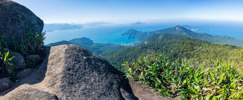 Luscious green mountains beside a calm blue sea under a clear sky.