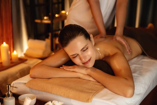 Caucasian woman customer enjoying relaxing anti-stress spa massage and pampering with beauty skin recreation leisure in warm candle lighting ambient salon spa at luxury resort or hotel. Quiescent