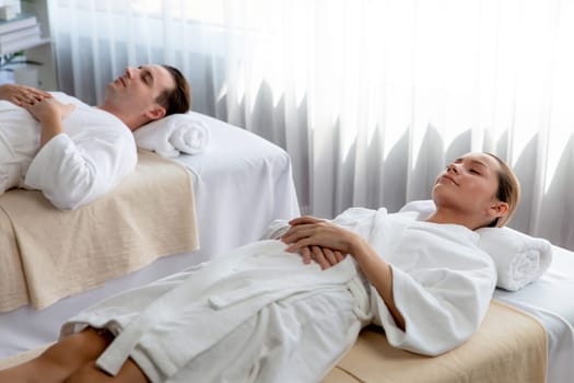 Caucasian couple customer enjoying relaxing anti-stress spa massage and pampering with beauty skin recreation leisure in day light ambient salon spa at luxury resort or hotel. Quiescent