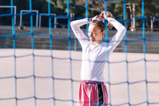 smiling female soccer player making a ponytail to play on an urban football court, concept of sport and active lifestyle, copy space for text