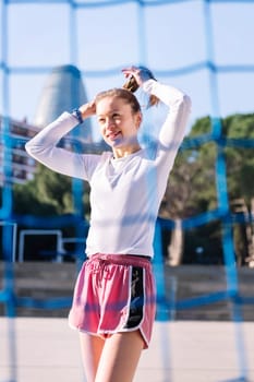 smiling female soccer player making a ponytail to play on an urban football court, concept of sport and active lifestyle