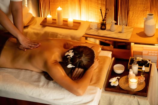 Caucasian woman customer enjoying relaxing anti-stress spa massage and pampering with beauty skin recreation leisure in warm candle lighting ambient salon spa at luxury resort or hotel. Quiescent