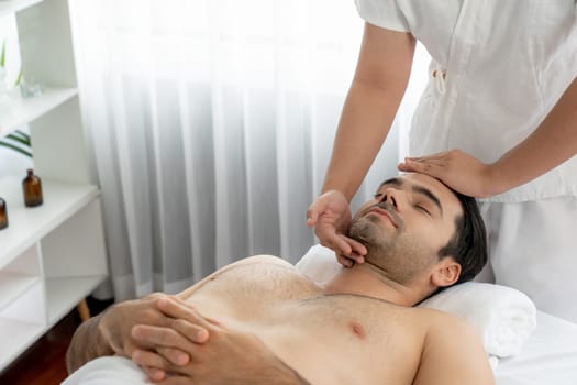 Caucasian man enjoying relaxing anti-stress head massage and pampering facial beauty skin recreation leisure in dayspa modern light ambient at luxury resort or hotel spa salon. Quiescent