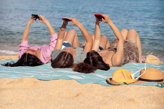 Three young women using apps on their cell phones on the beach