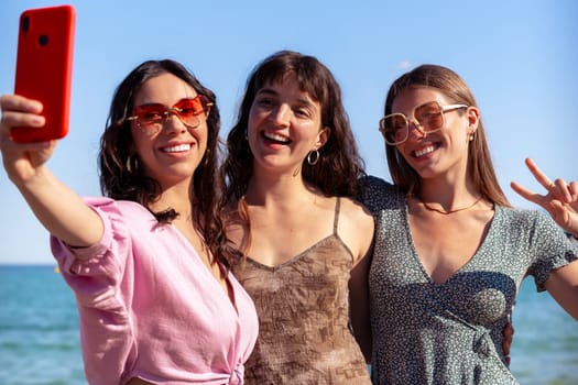 Group of smiling multiethnic women enjoying vacation. Beautiful and cheerful girls of generation z pose for a photo with a mobile phone.