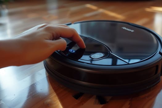 A woman's hand turns on a robot vacuum cleaner on the wooden floor in the room.