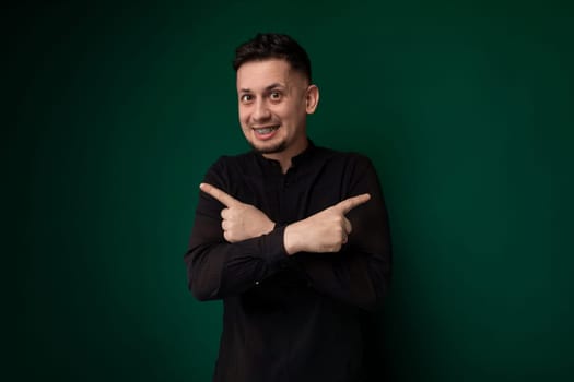 A man wearing a black shirt is pointing at an object or direction, showing emphasis or interest in a specific subject. His gesture suggests urgency or importance in his communication.