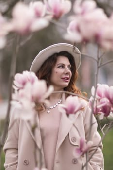 Woman magnolia flowers, surrounded by blossoming trees, hair down, white hat, wearing a light coat. Captured during spring, showcasing natural beauty and seasonal change