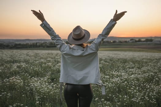 A woman wearing a hat stands in a field of flowers, with her arms raised in the air. Concept of freedom and joy, as the woman is celebrating or expressing her happiness