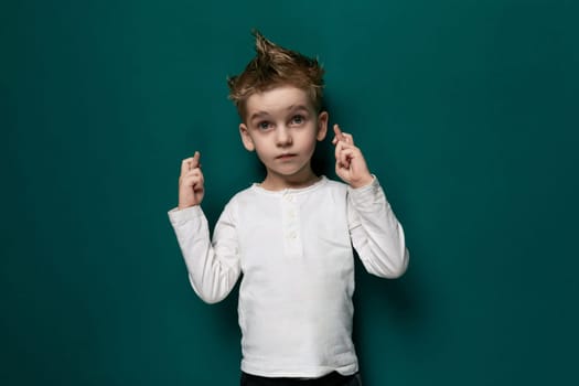 A young boy with a disheveled haircut stands in front of a vivid green wall. He appears curious and engaged in his surroundings, with a hint of mischief in his expression.