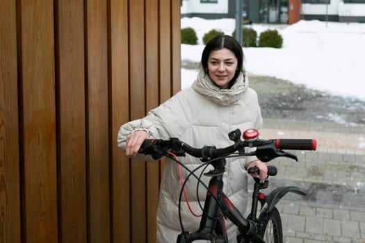 A woman standing next to a bicycle parked in a snowy landscape. She is wearing winter clothing as she surveys the winter scenery around her.