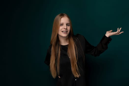 A woman with vibrant, long red hair stands confidently in front of a solid green wall, her presence commanding attention. Her hair cascades down her back, drawing eyes towards her elegant posture.