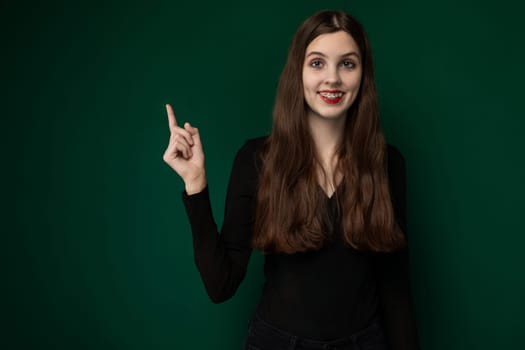 A woman wearing a black shirt is raising her hand to make a peace sign gesture. Her fingers are forming the V-shape commonly associated with peace and victory signs.