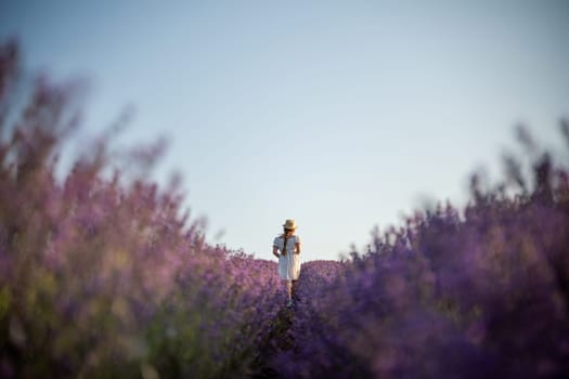 Lavender field girl. Back view happy girl in white dress with a scythe runs through a lilac field of lavender. Aromatherapy travel.