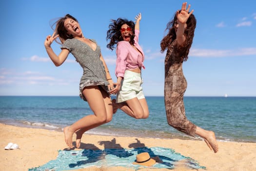 Three happy girls in jumping motion with on the beach outdoors in summer celebrating vacation days. Friends having fun on vacation by the sea carefree, and party concept