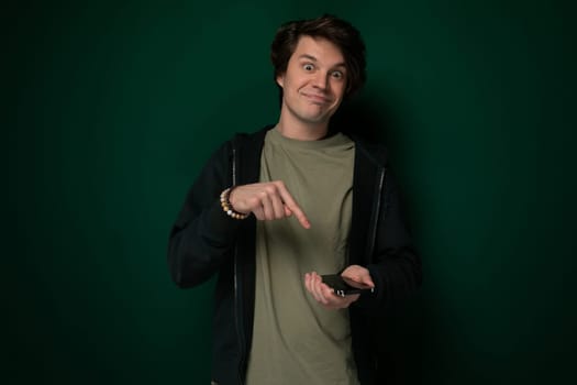 A man standing in front of a green wall, pointing at an unseen object with his index finger. He appears focused and engaged in the act of pointing towards something of interest.