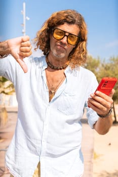 Caucasian man wearing sunglasses feeling angry showing his finger down in disapproval outdoors.