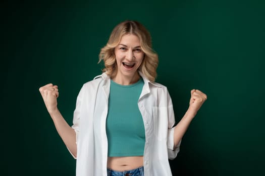 A woman dressed in a green top and white jacket standing outdoors. She looks stylish and confident as she poses for a photo.