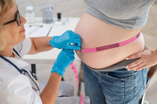 Doctor measuring the volume of a pregnant woman's abdomen using a centimeter tape