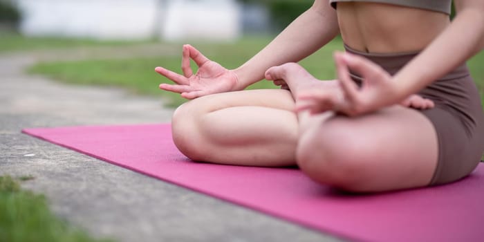 Woman practice yoga on a pink mat in a park, focusing on stretching and meditation for a healthy lifestyle.