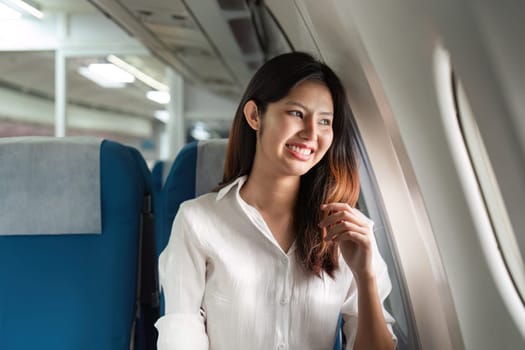 Businesswoman in a white shirt, smiling and looking out the window of a modern business airplane, seated in a luxurious cabin.