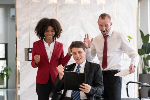 Diverse business team of three people, including a woman and two men, celebrating positive financial report results at an office desk with a laptop and paperwork, bright modern office setting