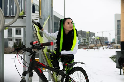 A woman is standing next to a bicycle in the snow. She looks bundled up for the cold weather, with snow covering the ground around her.