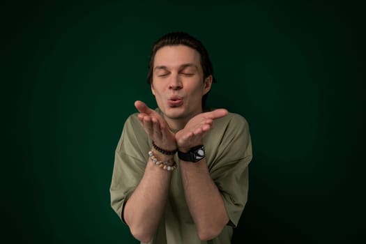 A man is standing in front of a green background, holding his hands together. He appears relaxed and focused, with a neutral expression. The background is a solid shade of green, providing a simple backdrop for the mans pose.