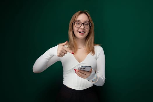 A woman wearing glasses is seen holding a cell phone in her hand. She appears focused on the screen, possibly texting or browsing. The background is simple and non-distracting.