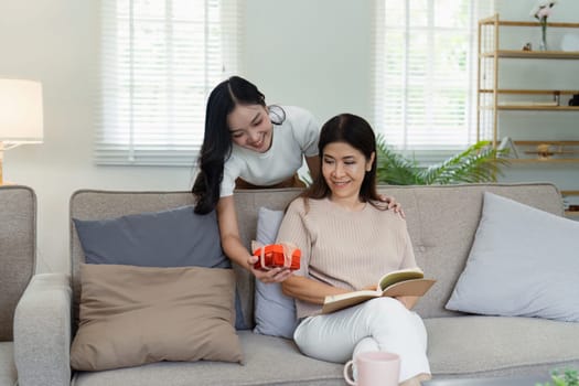 A joyful mother and daughter celebrating Mother's Day at home, sharing a special gift on a cozy sofa in a bright and modern living room.