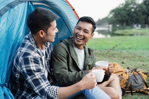 Couple gay lgbt enjoying morning coffee in front of a tent by a scenic lakeside, embodying the spirit of travel camping and outdoor adventure.