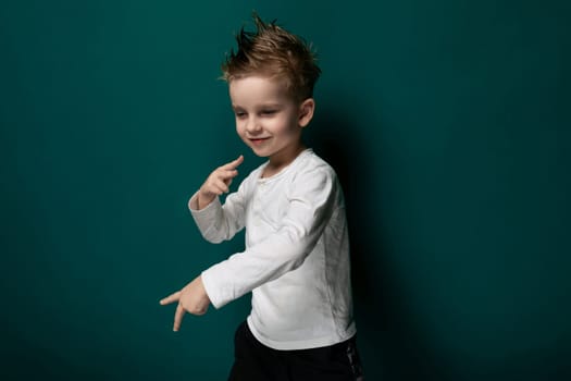 A young boy stands in front of a vibrant green wall, looking ahead with a curious expression. His hands are relaxed by his side as he takes in his surroundings.