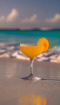 Tropical cocktail with orange slice on sandy beach, clear blue sea and sky in background.