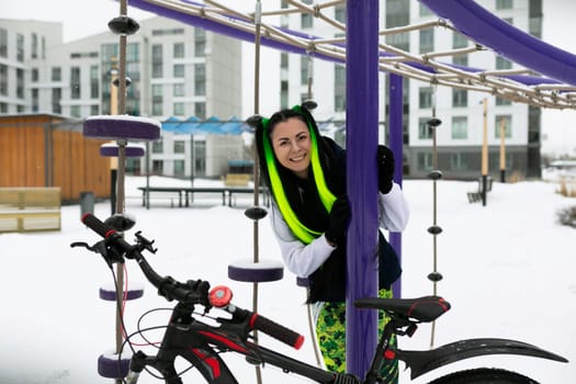 A woman standing next to a bicycle in a snowy landscape. She is wearing winter clothing and appears to be adjusting something on the bike.