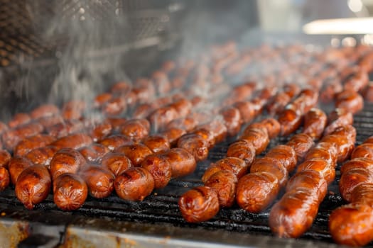 Grilled sausages on a barbecue with rising smoke, indicating an outdoor cookout.