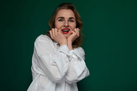 A woman wearing a white shirt stands with her hands on her face, striking a pose for the camera.