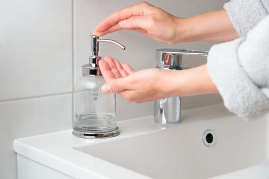 Cropped shot of woman using liquid soap from dispenser bottle for washing hands procedure at domestic bathroom. Female applying sanitizer gel or antibacterial cleanser. Hygiene concept