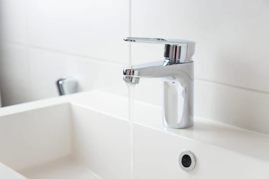 Modern bathroom faucet, water tap with running water and white sink, pure water concept, saving natural recourses concept banner with copy space