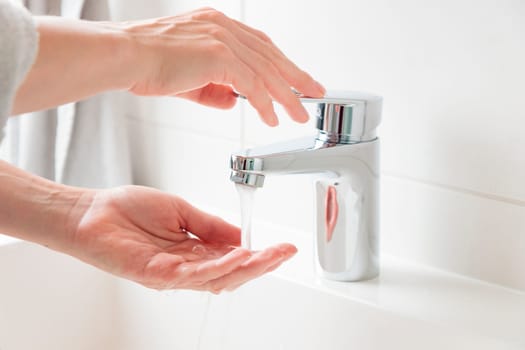 Woman is opening and closing water flow tap and filling water temperature. Water running from chrome faucet. Bathroom plumbing. Using water resources concept