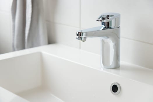 A drop of pure water dripping from the tap in the white modern bathroom. Clean tap water concept. Wise use of natural resources.